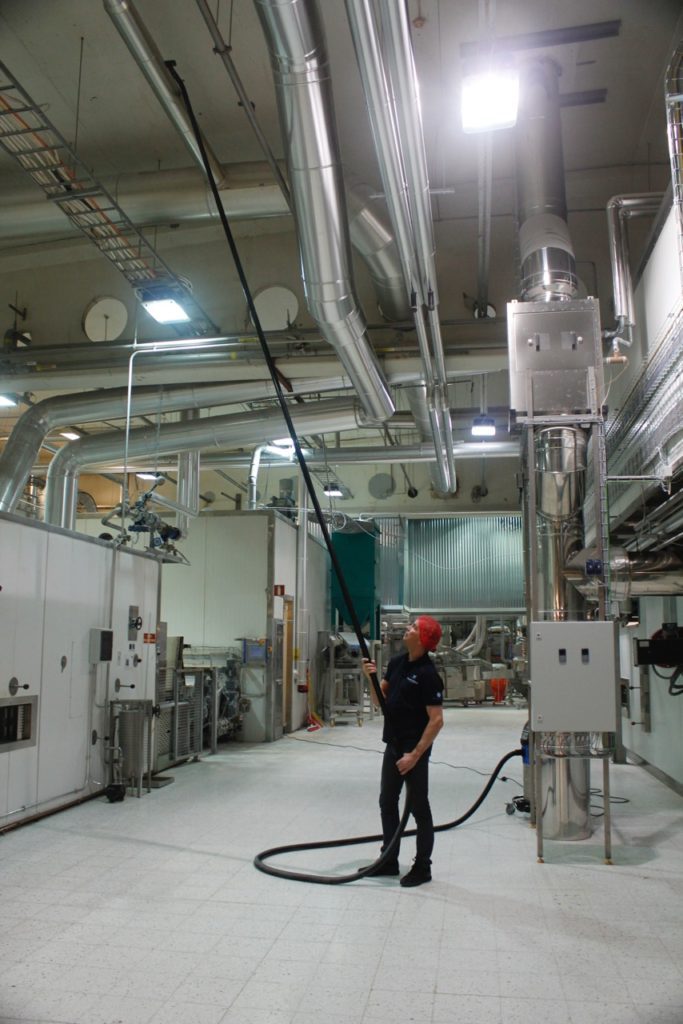 A Technician vacuuming Combustible Dust located overhead, in a manufacturing facility